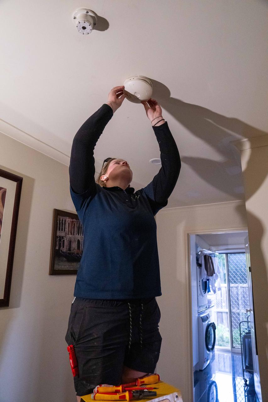 Goldsure electrician on a ladder fitting a smoke alarm